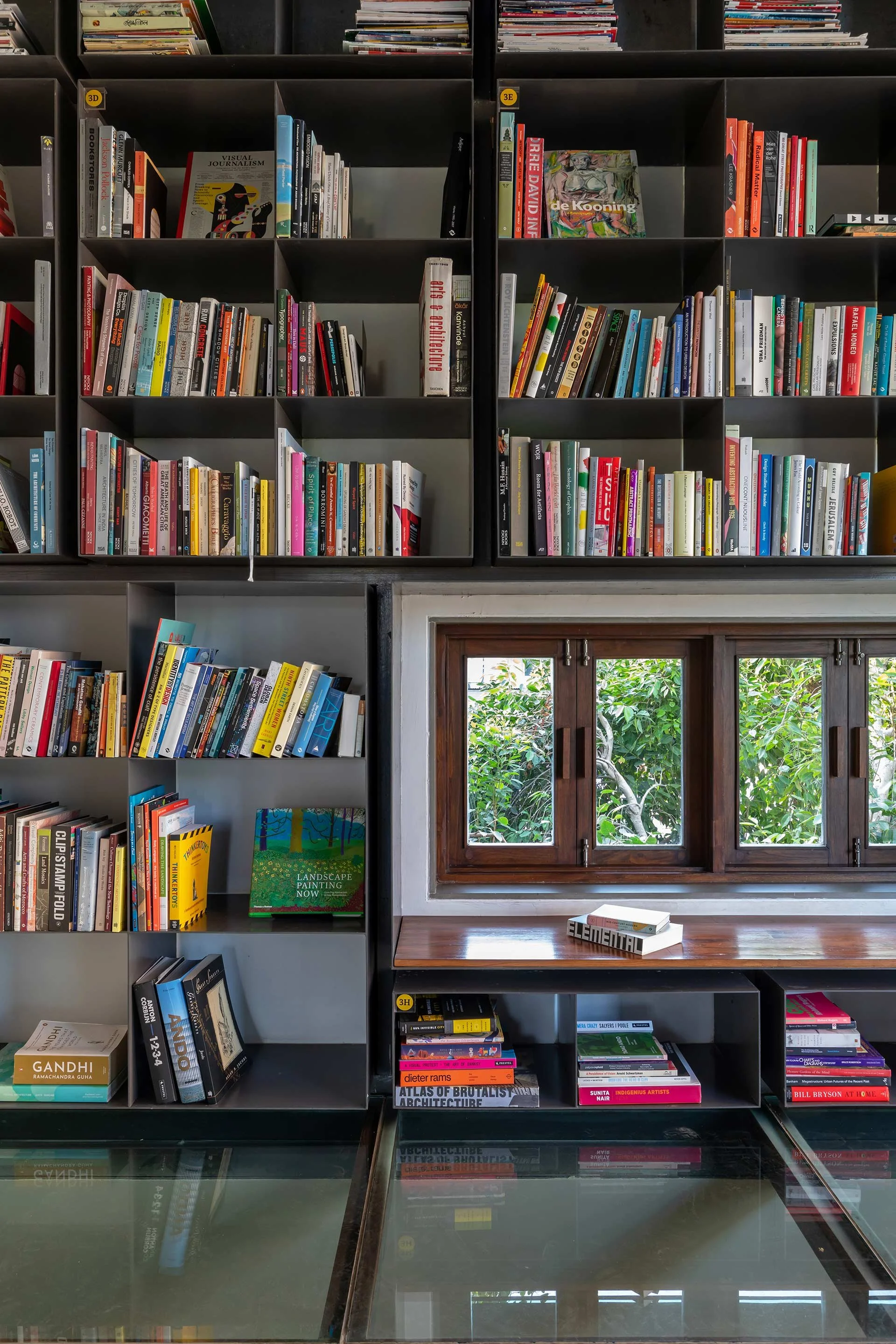 Bookshelves filled with books, a small window showing greenery outside, and a glass table with books on it. in Ahmedabad, photographed by Rishul Bangar.
