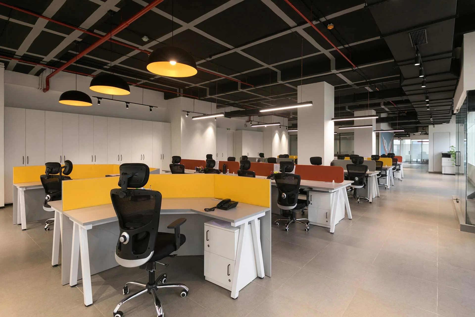 Empty modern office with workstations, black ergonomic chairs, colorful privacy dividers, and ceiling lighting