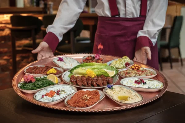 Ein Kellner trägt einen großen runden Teller mit traditionellen türkischen Meze-Gerichten in einem Restaurant.