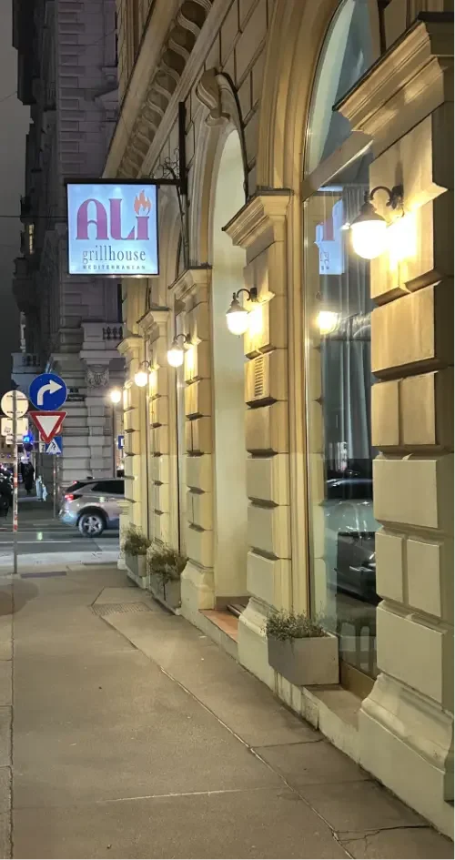 Straßenansicht vor einem Restaurant namens ALI Grillhouse bei Nacht mit beleuchteten Fenstern und Hinweistafeln.