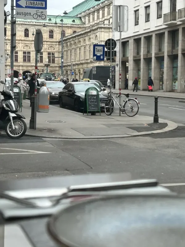 Blick von Restaurant Ali Grillhouse auf die Wiener Staatsoper. Blick von der Elisabethstrasse mitten in der Stadt Wien mit Parkplätzen, Fahrrädern, Autos und Passanten
