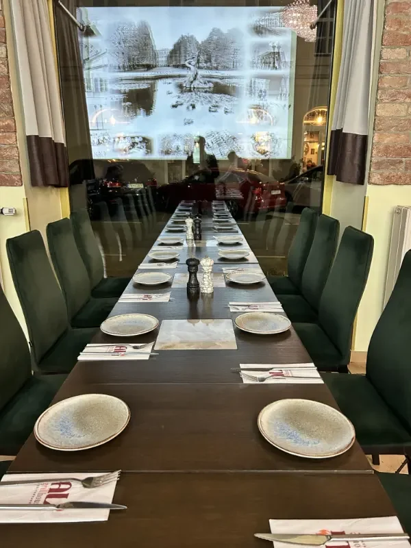 Ein langer Esstisch in einem Restaurant, gedeckt mit Tellern, Besteck, Salz- und Pfefferstreuern, vor großen Fenstern mit Blick auf eine verschneite Landschaft.