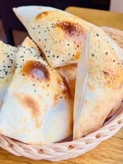 Gefüllte Teigtaschen mit schwarzen Mohnsamen in einem Korb auf einem Holztisch.