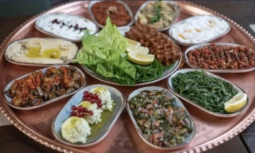 Verschiedene türkische Vorspeisen und Gerichte auf einem runden Tablett, inklusive Fladenbrot, grüner Salat, und geschnittenen Zitronen.