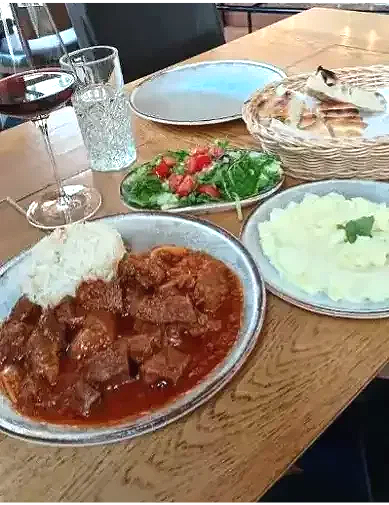 Deutsches Essen mit Fleisch in Sauce, Reis, Brot, Salat und Kartoffelpüree auf einem Holztisch.