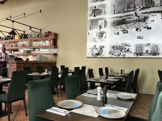 Innenansicht eines Restaurants mit dunkelgrünen Stühlen, gedeckten Tischen, einer Bar im Hintergrund und einem schwarz-weiß-Foto an der Wand.