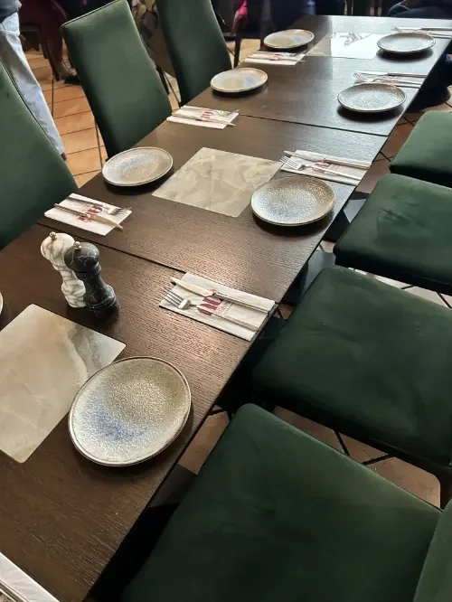 Ein Esstisch im Restaurant mit leeren Tellern, Besteck, Papptellern und Sitzgelegenheiten in Grün