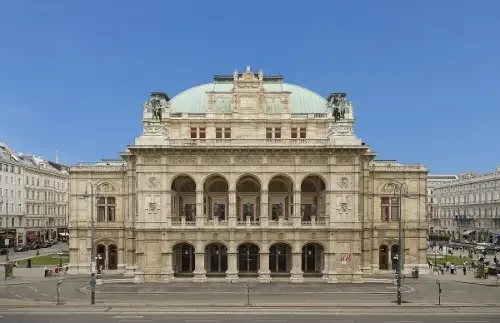 Ein klassisches Theatergebäude mit einer großen Fassade, mehreren Bögen und einem Kuppeldach unter klarem blauen Himmel.