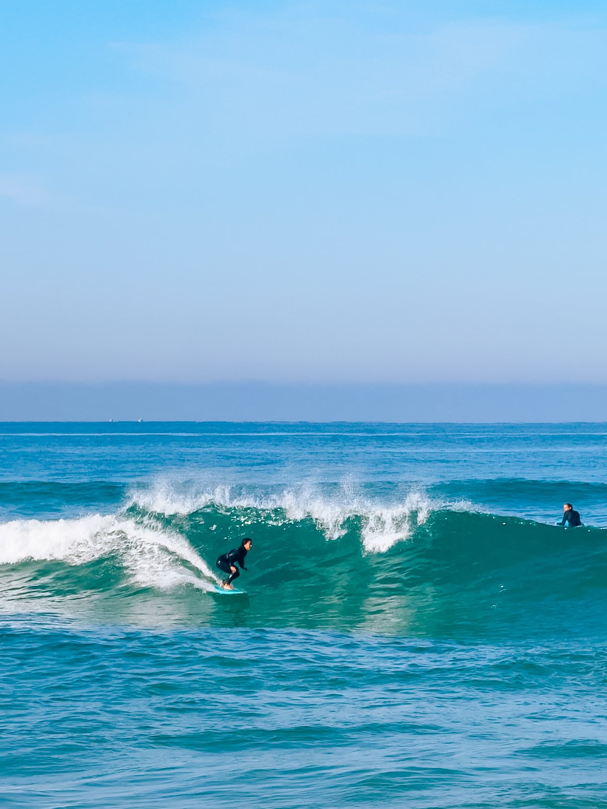 A person surfing on a wave in the ocean with another person in the background.