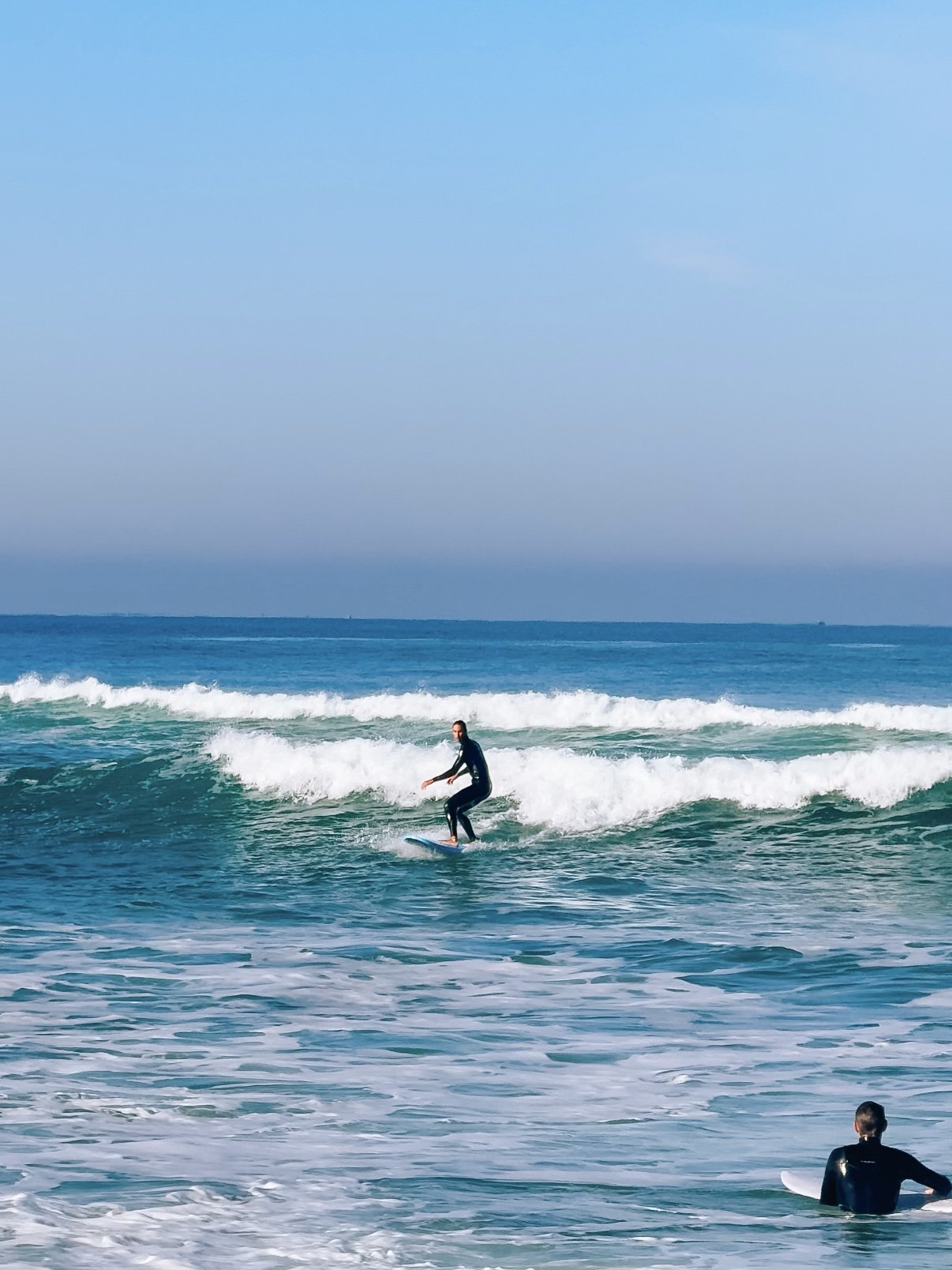 A person surfing on a wave in the ocean with another person sitting on a surfboard nearby.