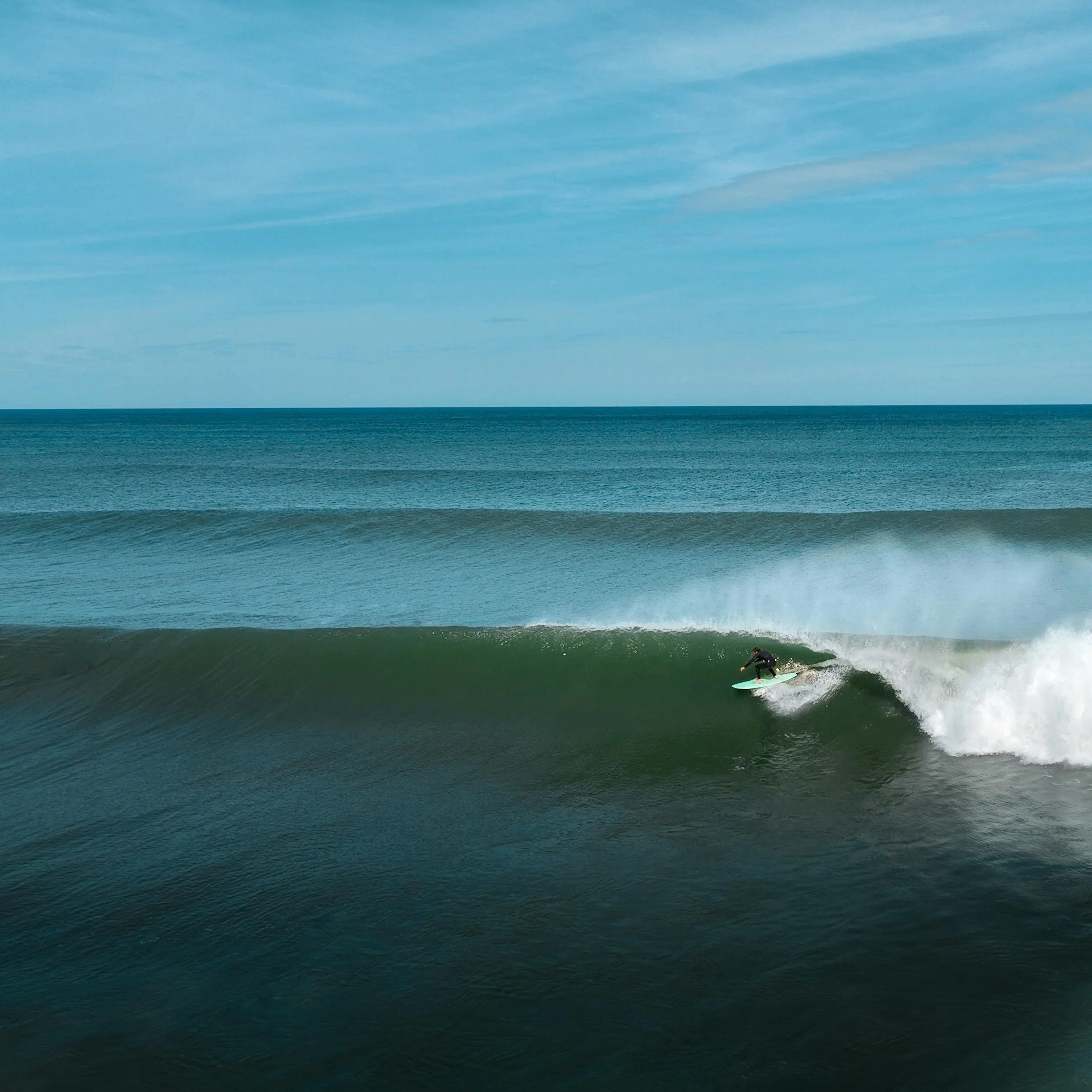 A person surfing on a wave in the ocean under a partly cloudy sky.
