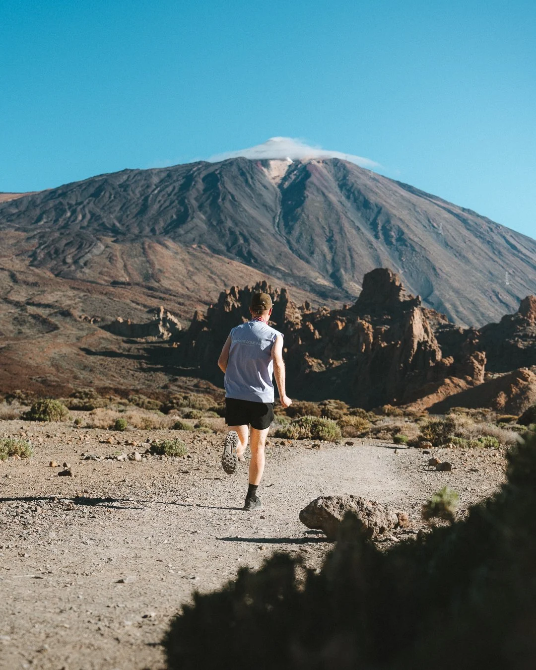 A person running on a dirt trail in a desert landscape with a large mountain and volcano in the background.