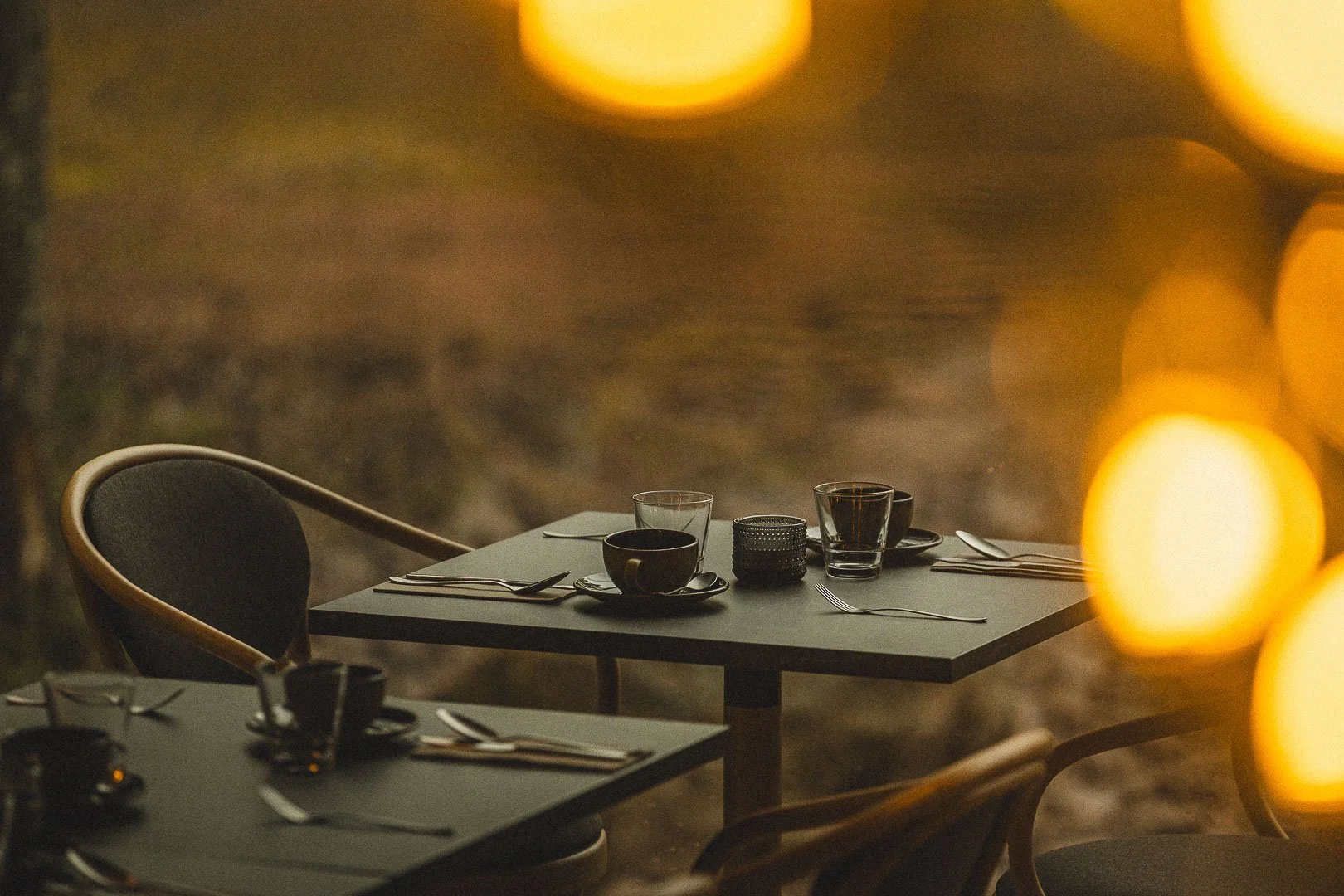 Ravintolapöytä ulkona illalla, asetellut lautaset, lasit ja veitset.