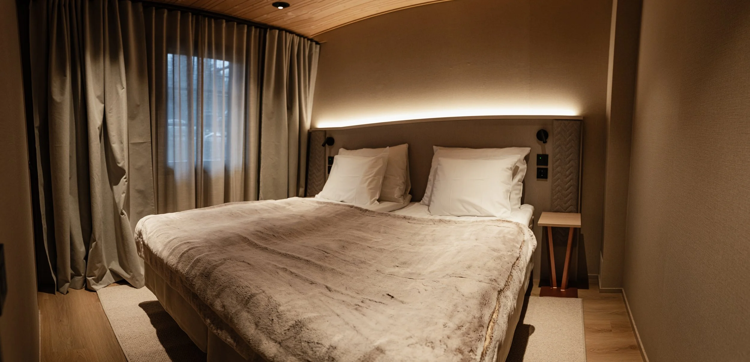 Yhden hengen makuuhuone, jossa suuri sänky, valkoiset tyynyt, pehmeä päiväpeite ja verhot ikkunassa.