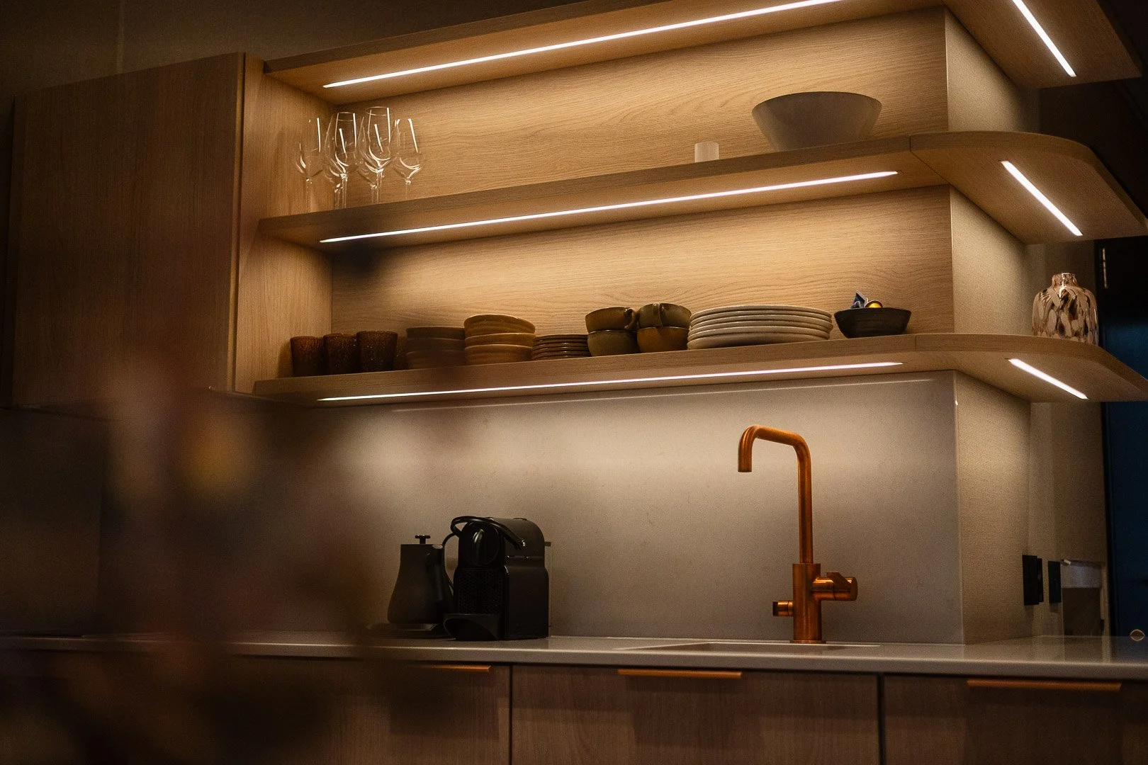 Moderni keittiö hyllyillä ja hanalla, jossa kahvikone ja vesihana.