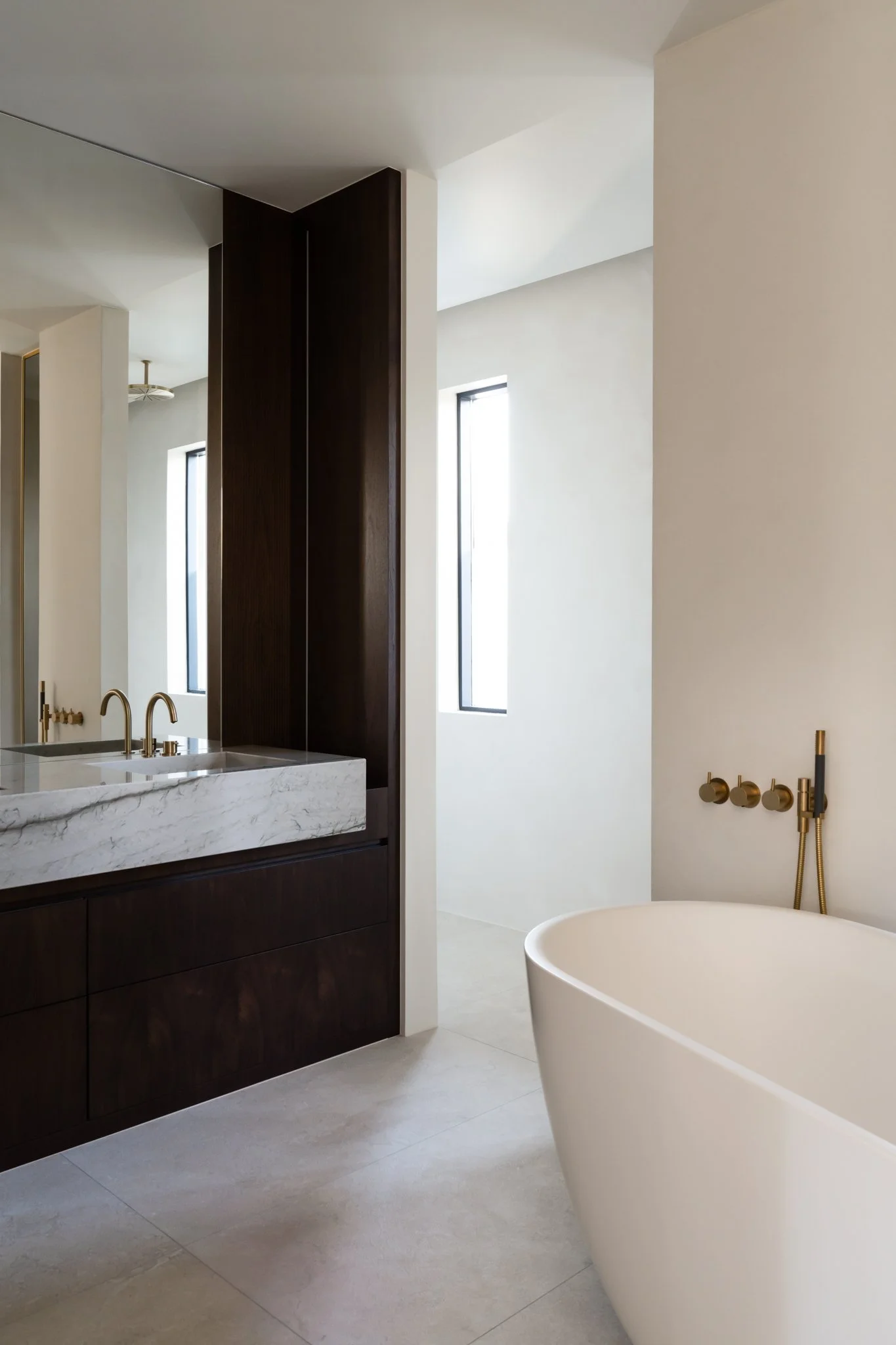 Modern bathroom with a freestanding white bathtub, dark wood vanity with marble countertop, and black-framed windows letting in natural light.