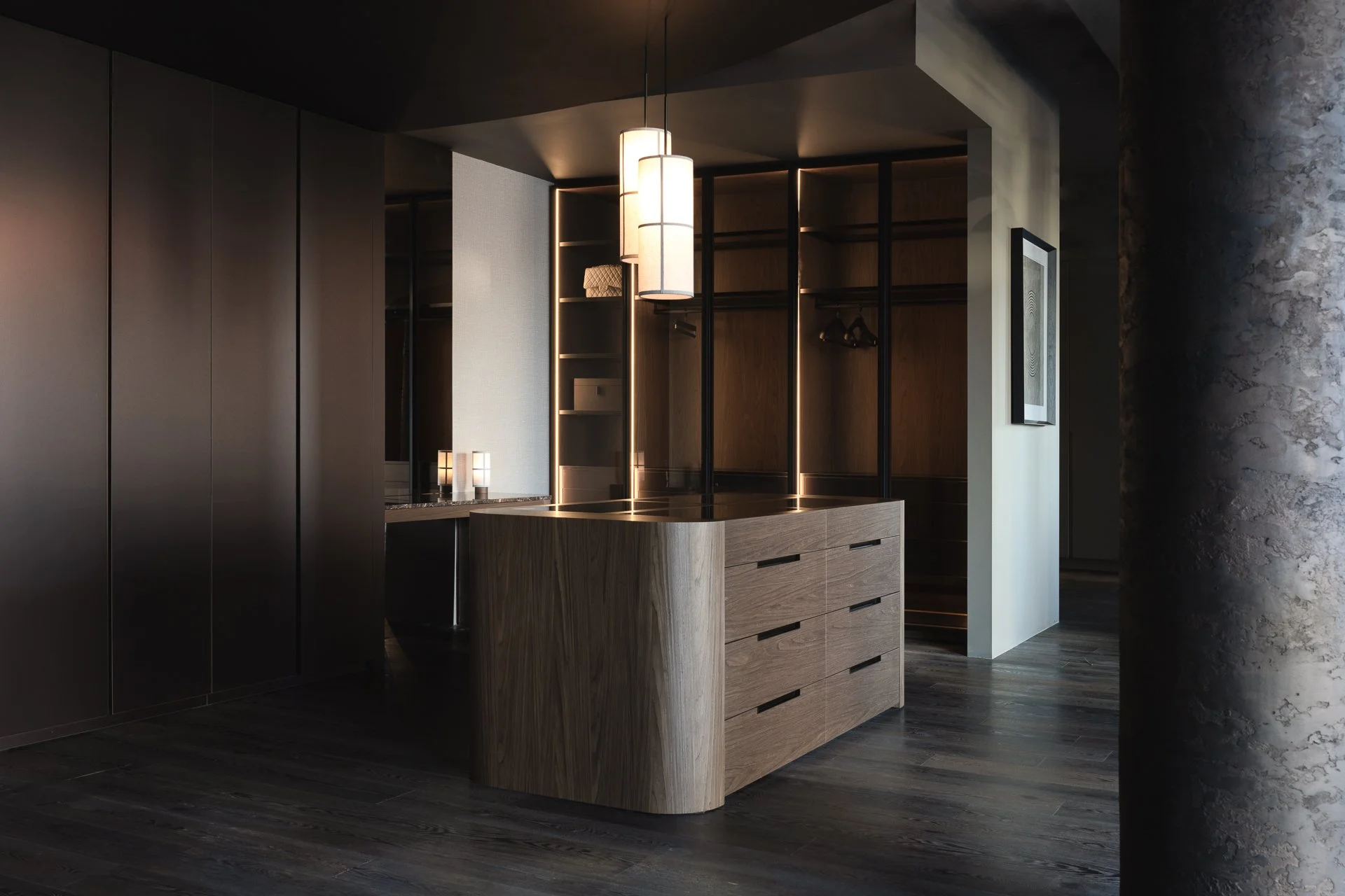 Modern interior with a wooden dresser, black and wood open closet, and hanging cylindrical pendant lights in a dimly lit room.