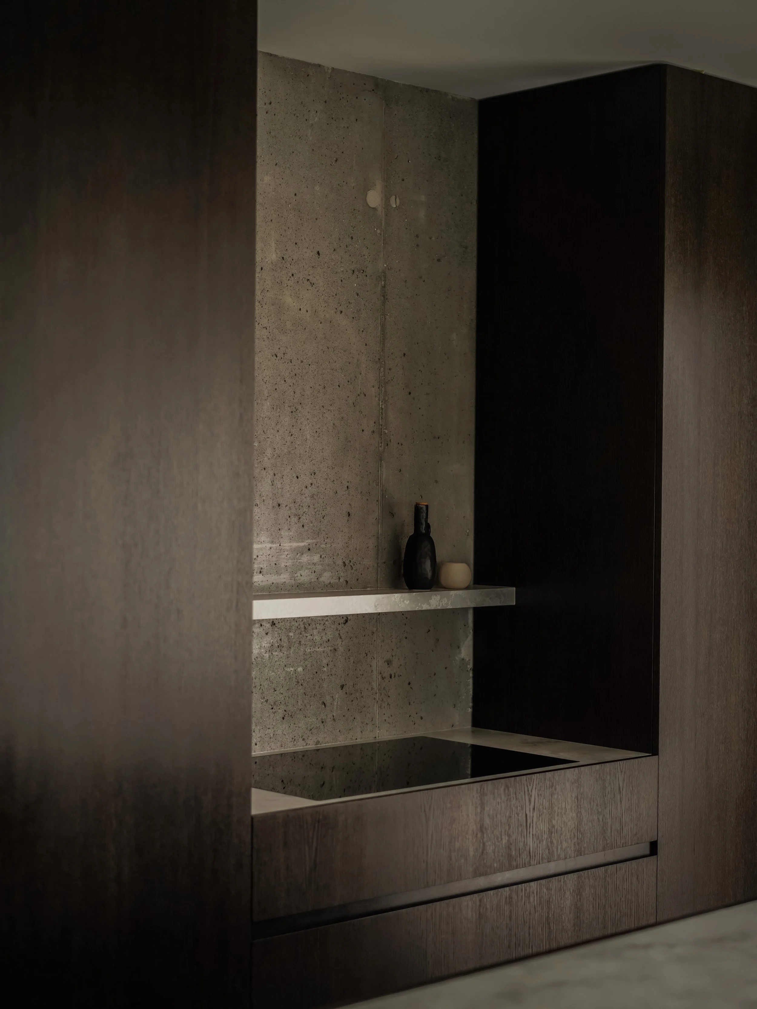 A minimalist bathroom shelf with two vases, one black and one beige, placed on a white shelf, against a concrete wall.