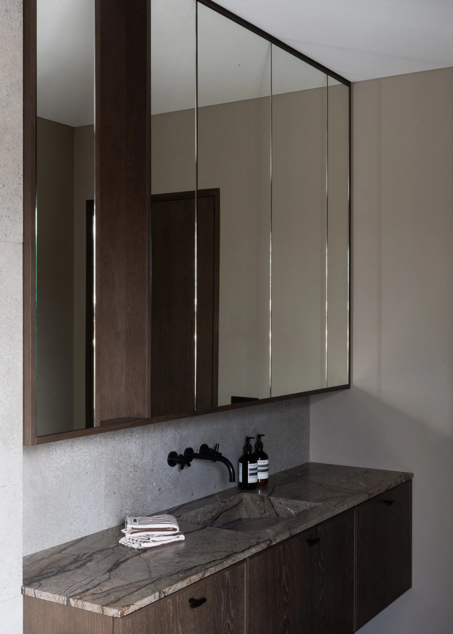 A modern bathroom vanity with a large mirror, dark wood cabinets, a marble countertop, a black faucet, and two bottles of hand soap.