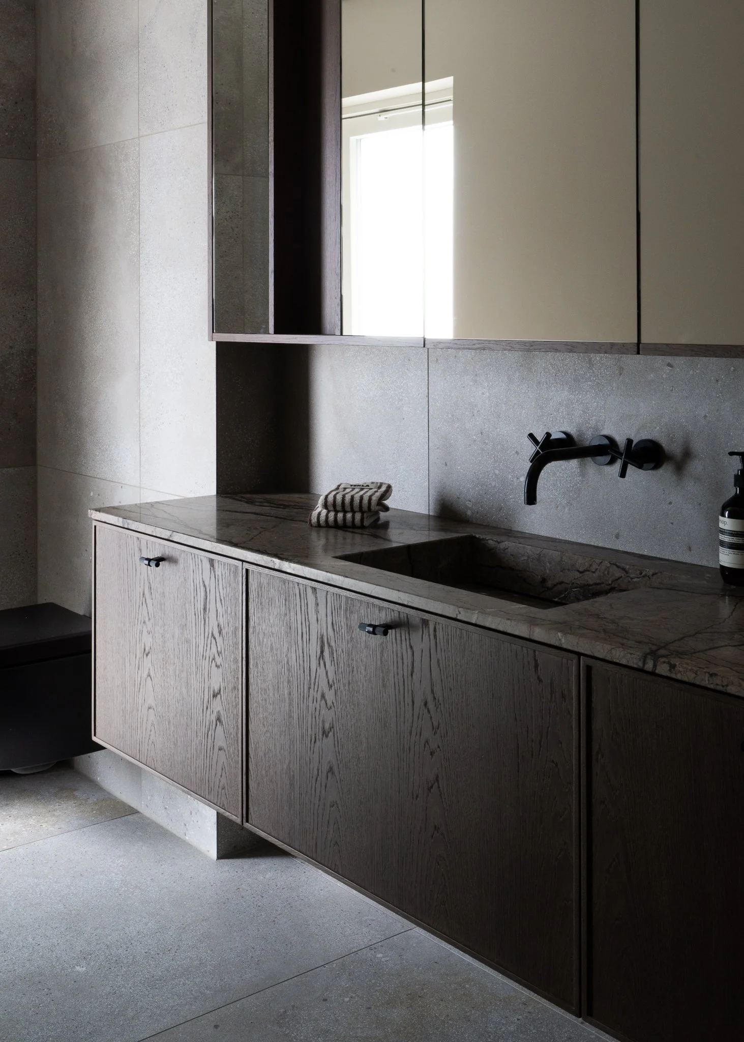 Modern bathroom with dark wood and beige cabinetry, marble countertop with a striped towel, black faucet, and a large mirror reflecting a window.