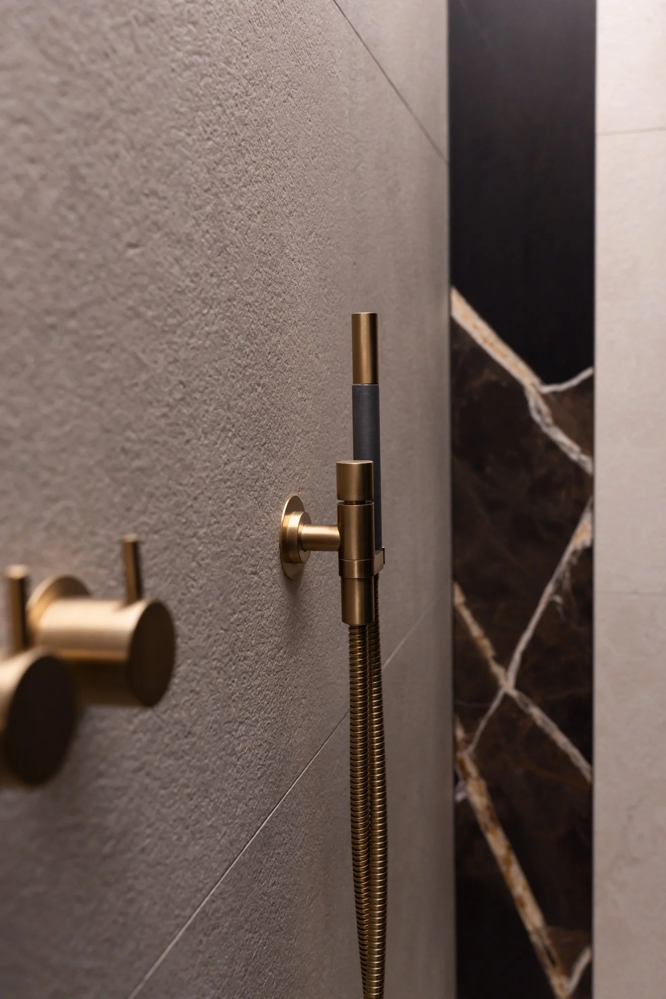 Close-up of a modern shower with a beige textured wall, a chrome shower hose, and black marble tiles with white veining.
