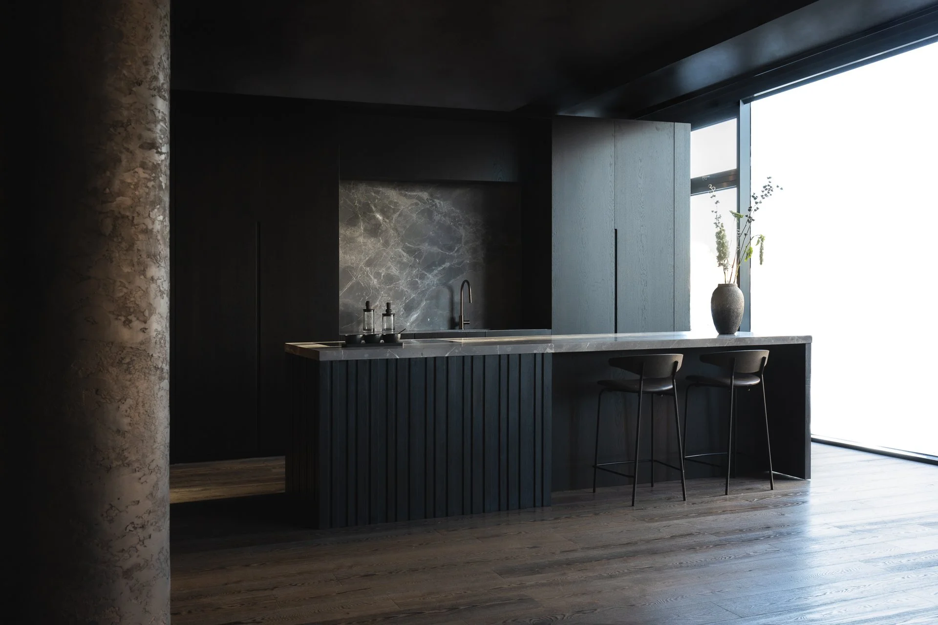 Modern kitchen with dark cabinetry, marble backsplash, and large window with a plant in a vase on the counter.