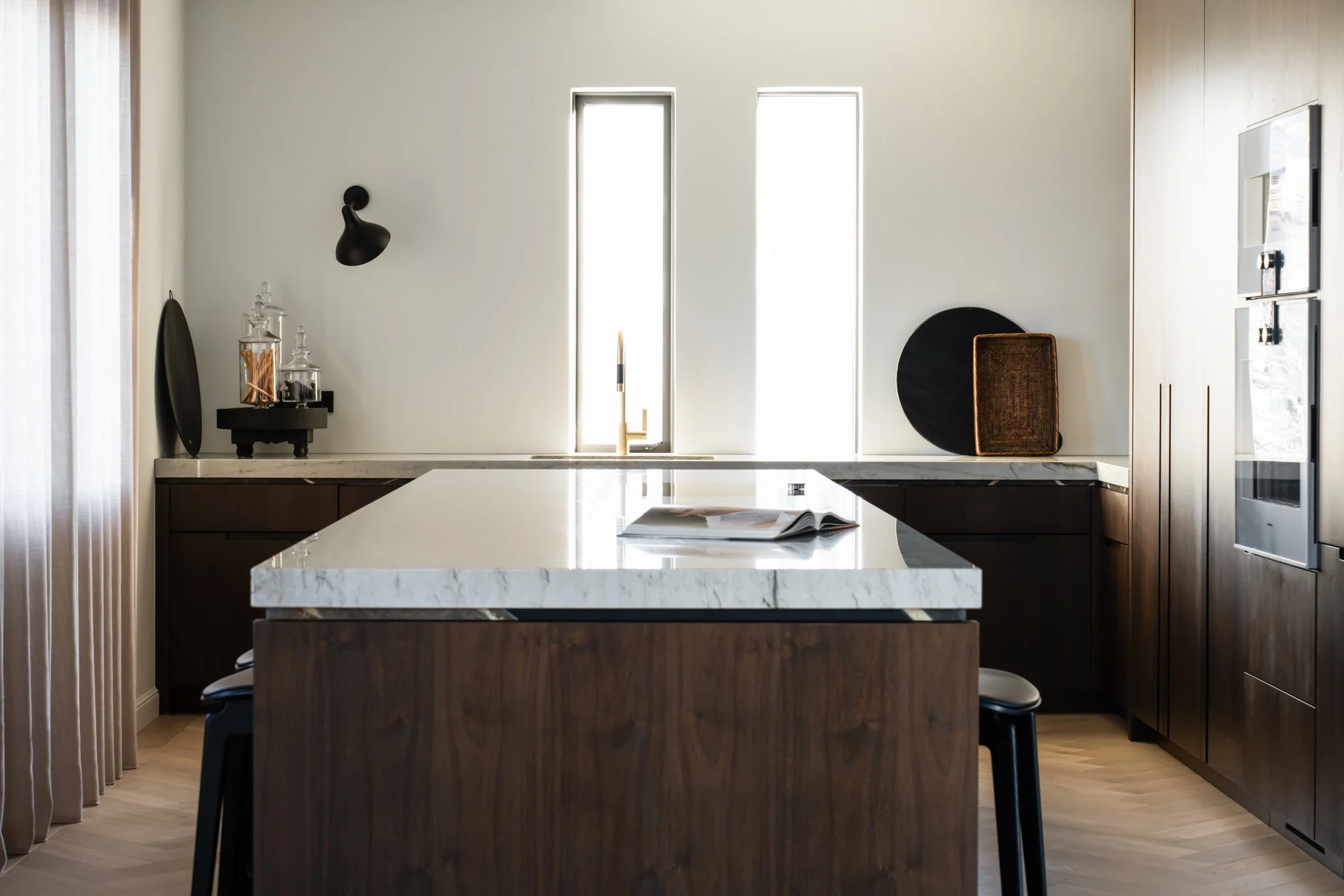 Modern kitchen with marble island, dark wood cabinets, minimal decor, and an open window letting natural light in.