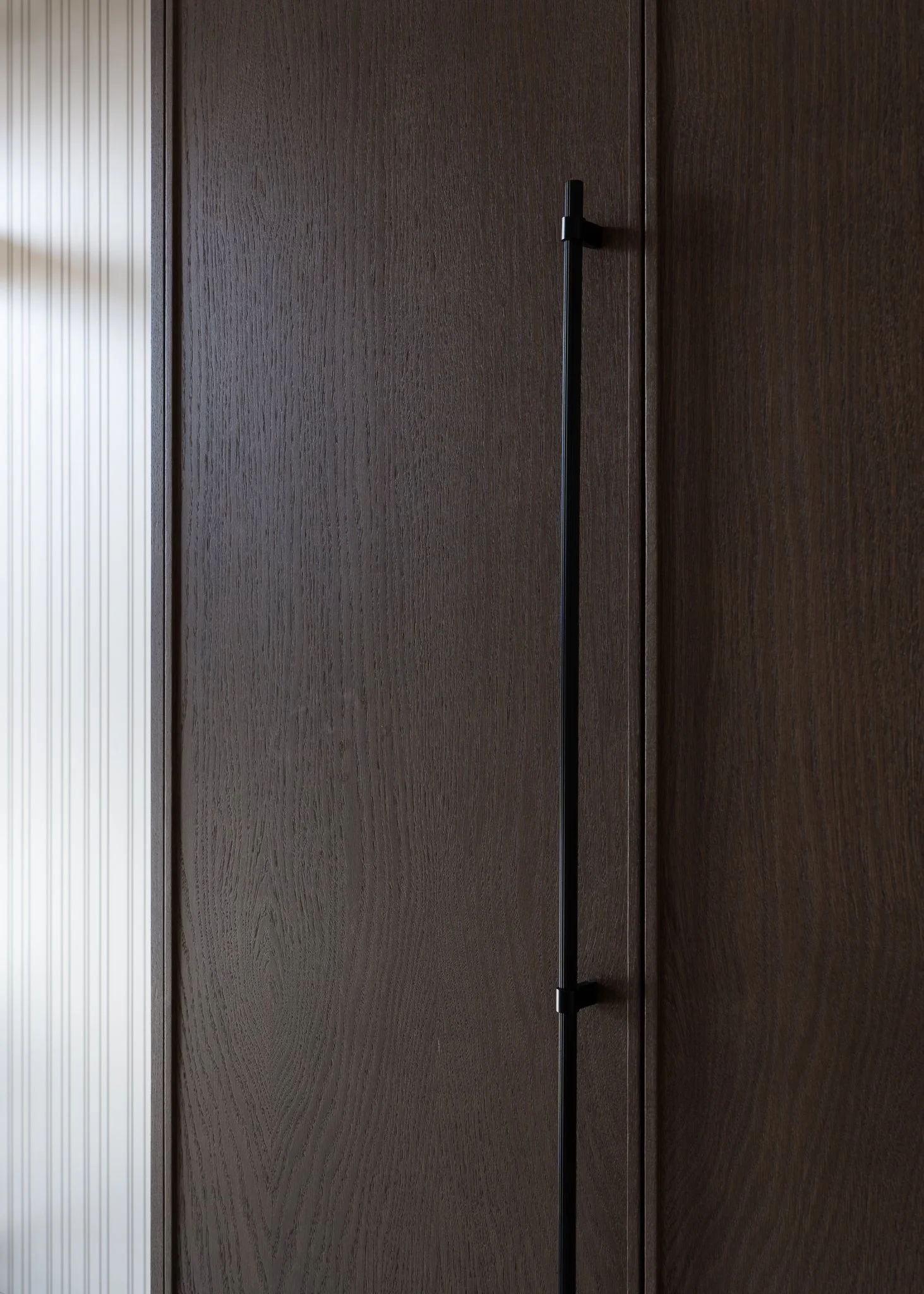 A dark brown wooden closet door with a black vertical handle in the middle.