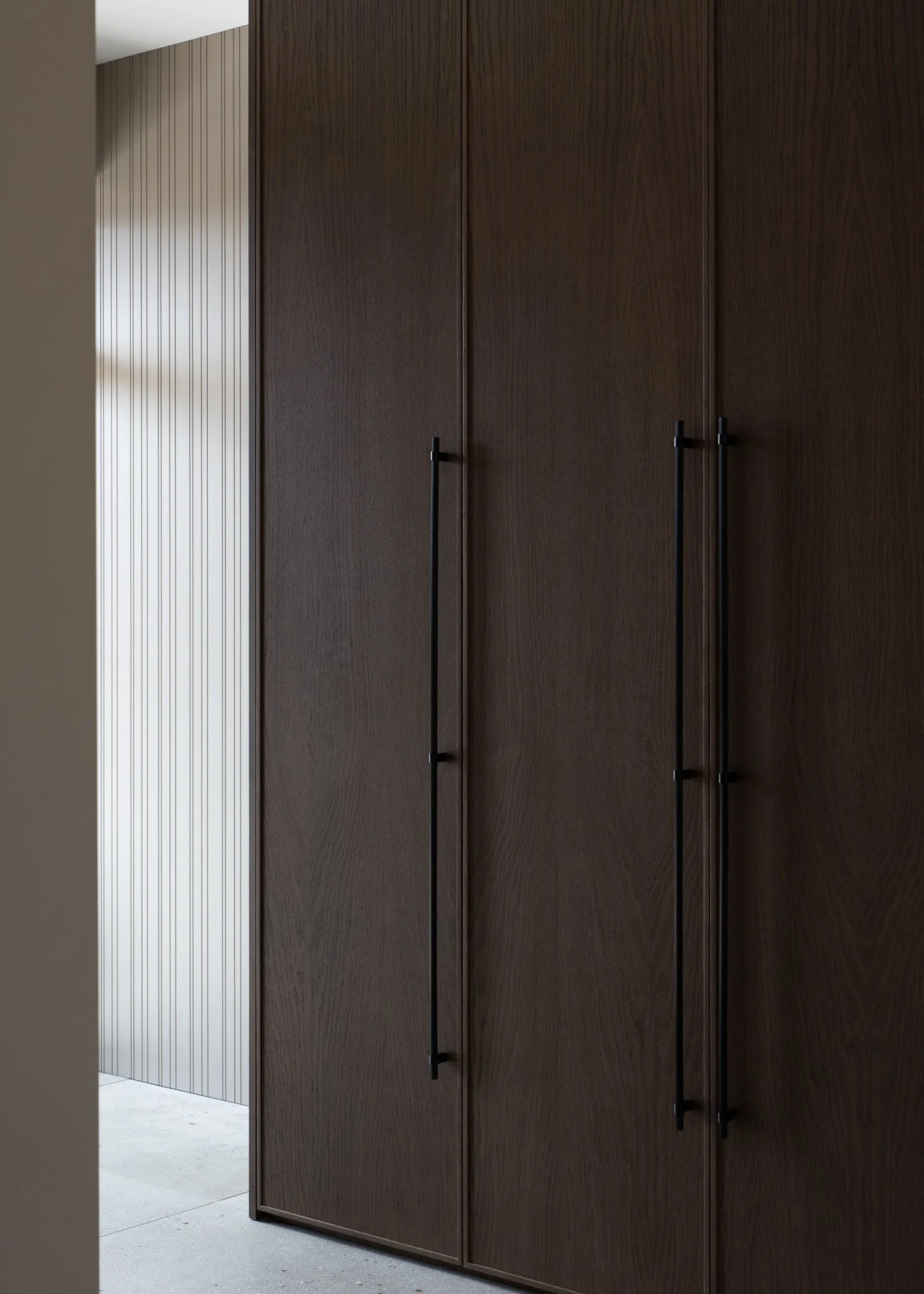 A modern closet with dark wood doors and black handles, with a light-colored wall and floor nearby.