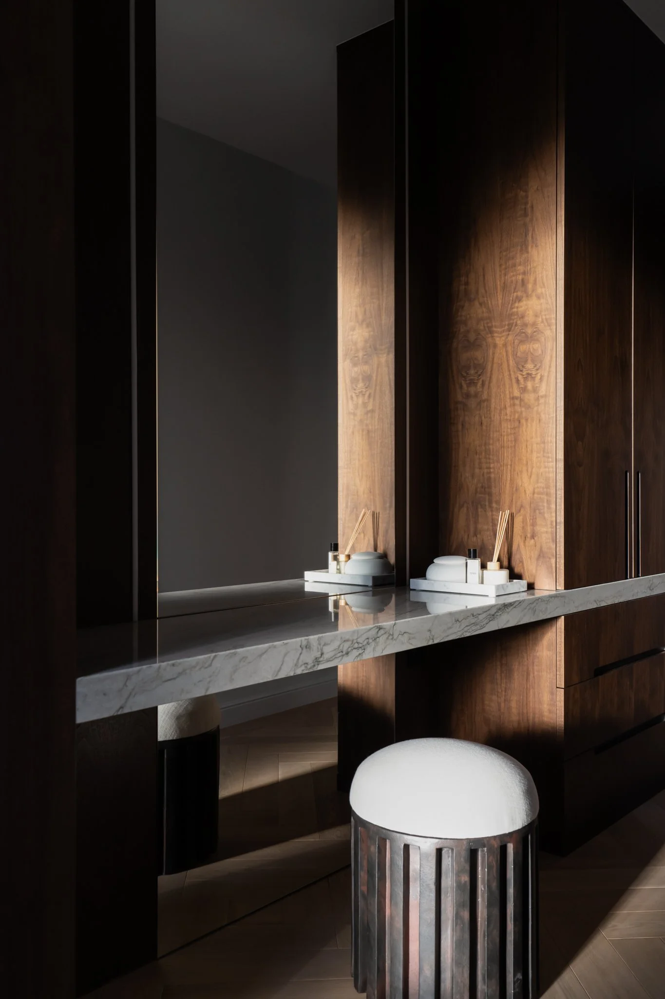 A bathroom vanity with a marble countertop, wooden cabinets, and a large mirror with decorative accessories such as reed diffusers on trays.