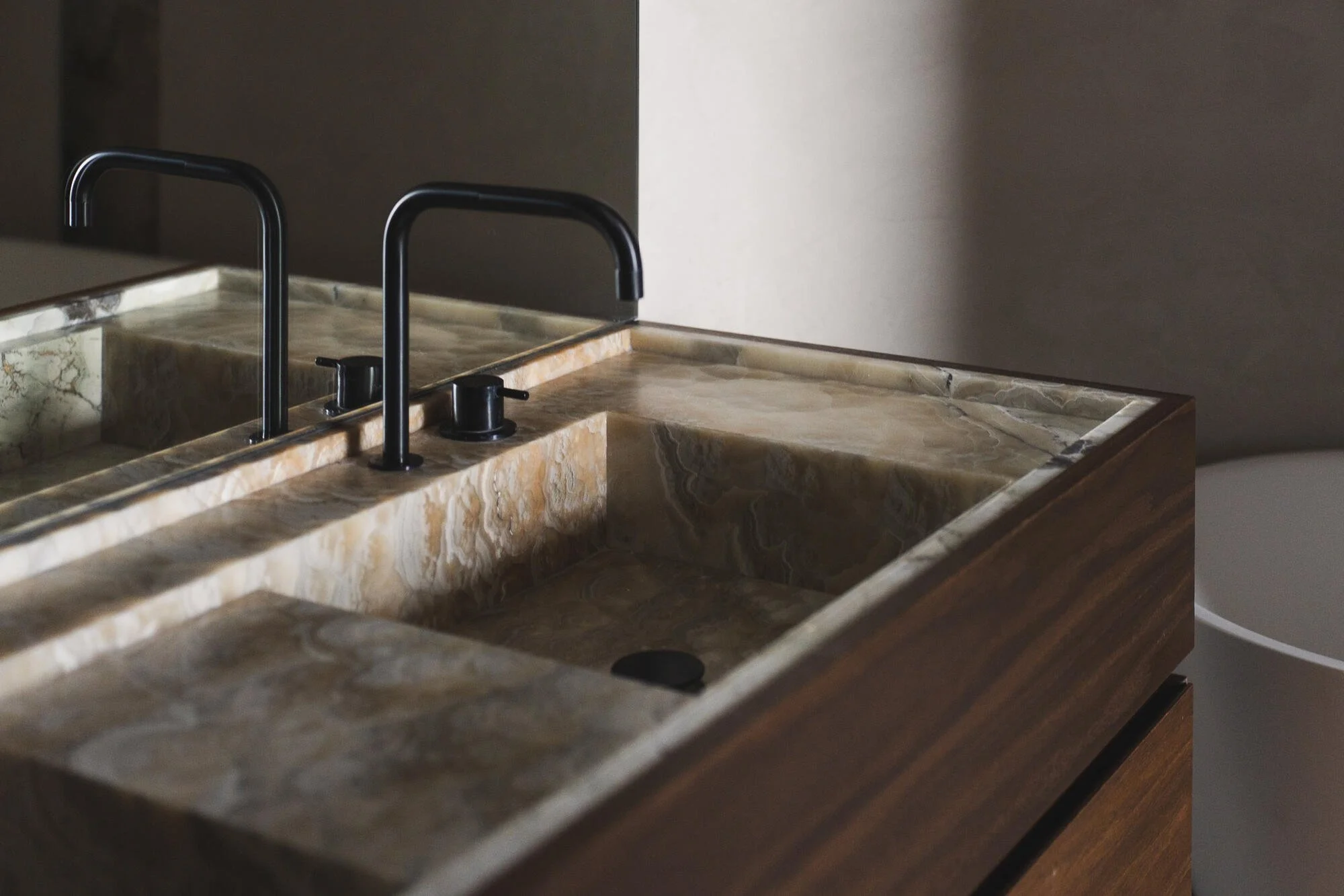Close-up of a marble kitchen sink with two black faucets and a backsplash, with a gray wall in the background.