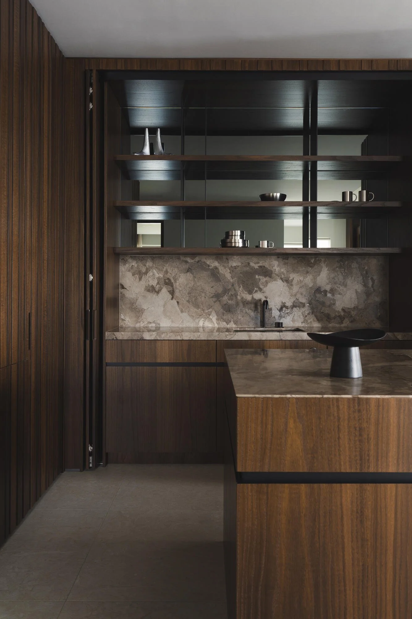 Modern kitchen with dark wood cabinetry, open shelves with metallic decorative items, marble backsplash, and a minimalist black faucet.