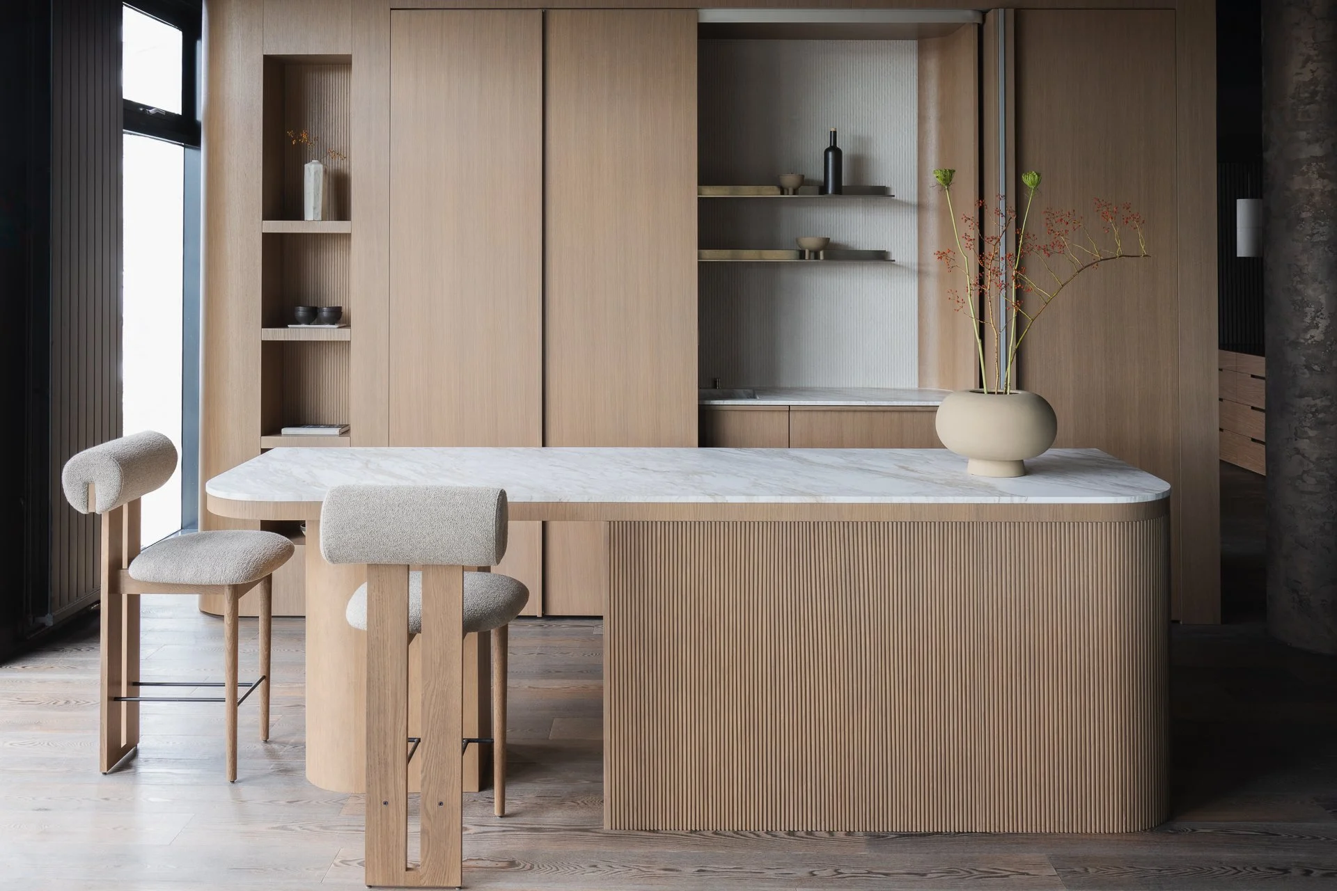 Modern kitchen with light wood cabinets, a white marble island, and a vase with red and green floral arrangement.