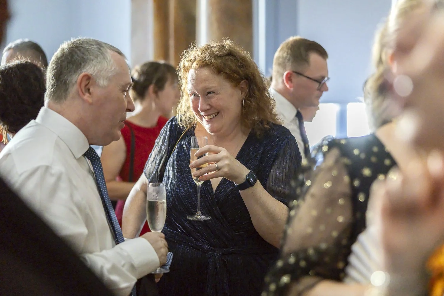 People socializing at a party, with a woman smiling while holding a glass of champagne.
