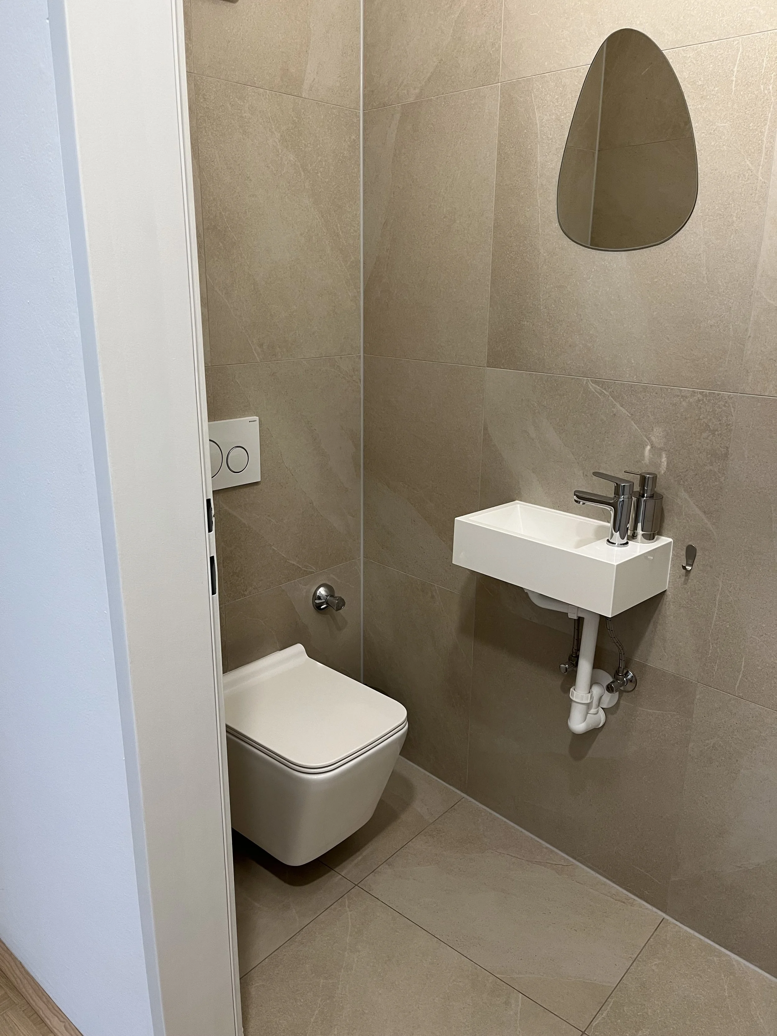 Moderne, minimalistische Toilette mit Wand-WC, rechteckigem Waschbecken und ovalem Spiegel.