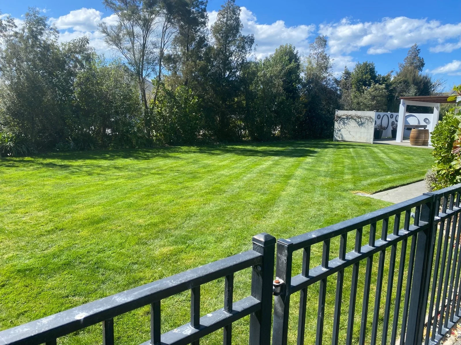 Large freshly mown lawn with visible mowing stripes, trees and boundary fencing at a Hawke's Bay property.