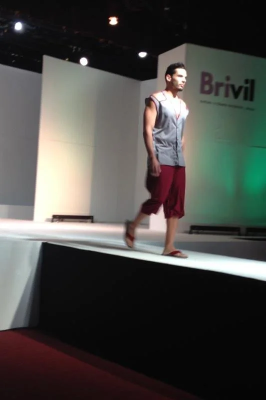 Male model walking on a runway at a fashion show with the Brivil logo in the background.