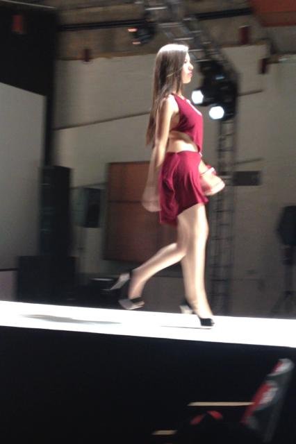 A young woman walking on a runway during a fashion show, wearing a red outfit.