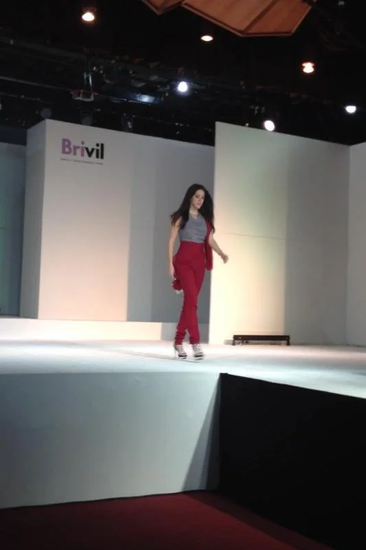 A woman walking on a stage at a fashion show, with a backdrop displaying the brand name "Brivil."