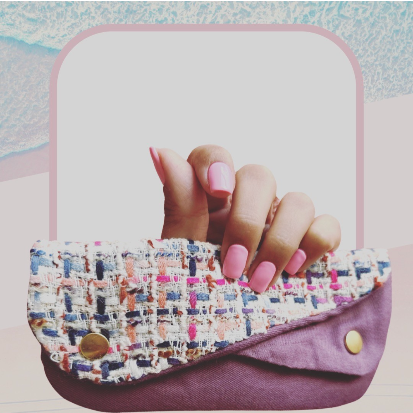 Close-up of a hand holding a purple purse with a multicolored tweed flap and gold button, with a background of sand and ocean waves.