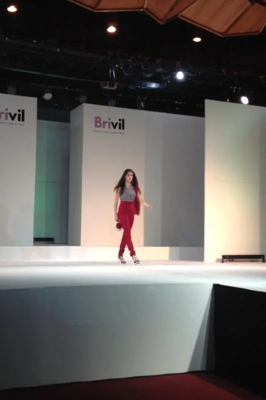 Female model walking on a runway during a fashion show, with a "Brivil" backdrop.
