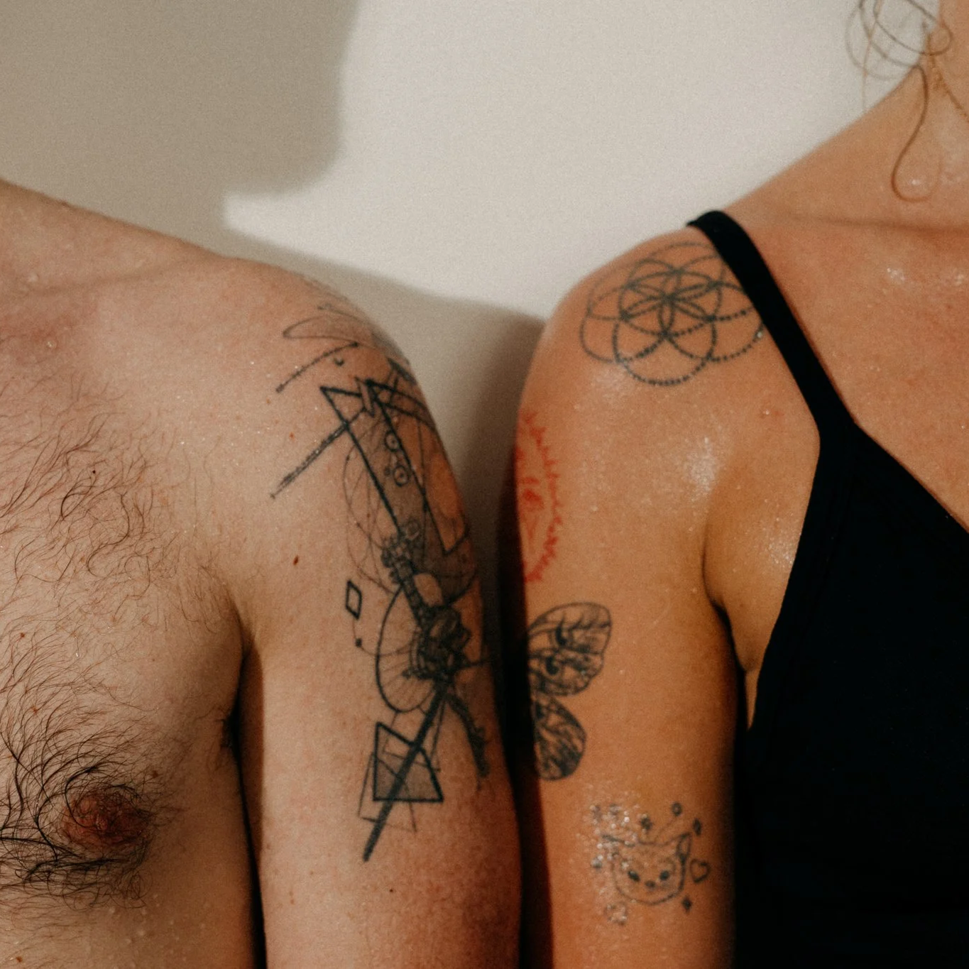Close-up of a man and woman showing their tattooed shoulders and arms, with some water droplets visible on their skin.