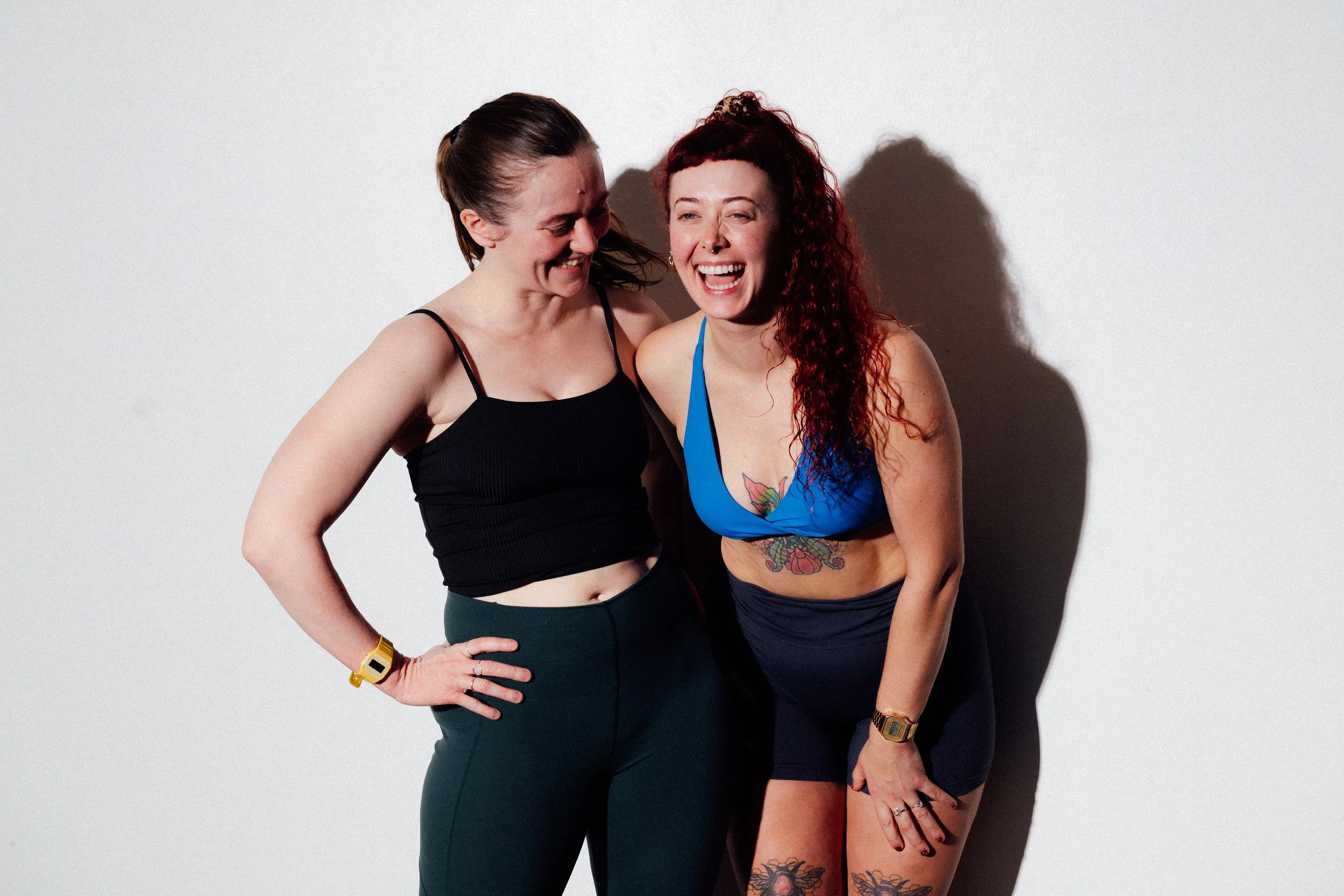 Two women laughing and hugging against a white background.