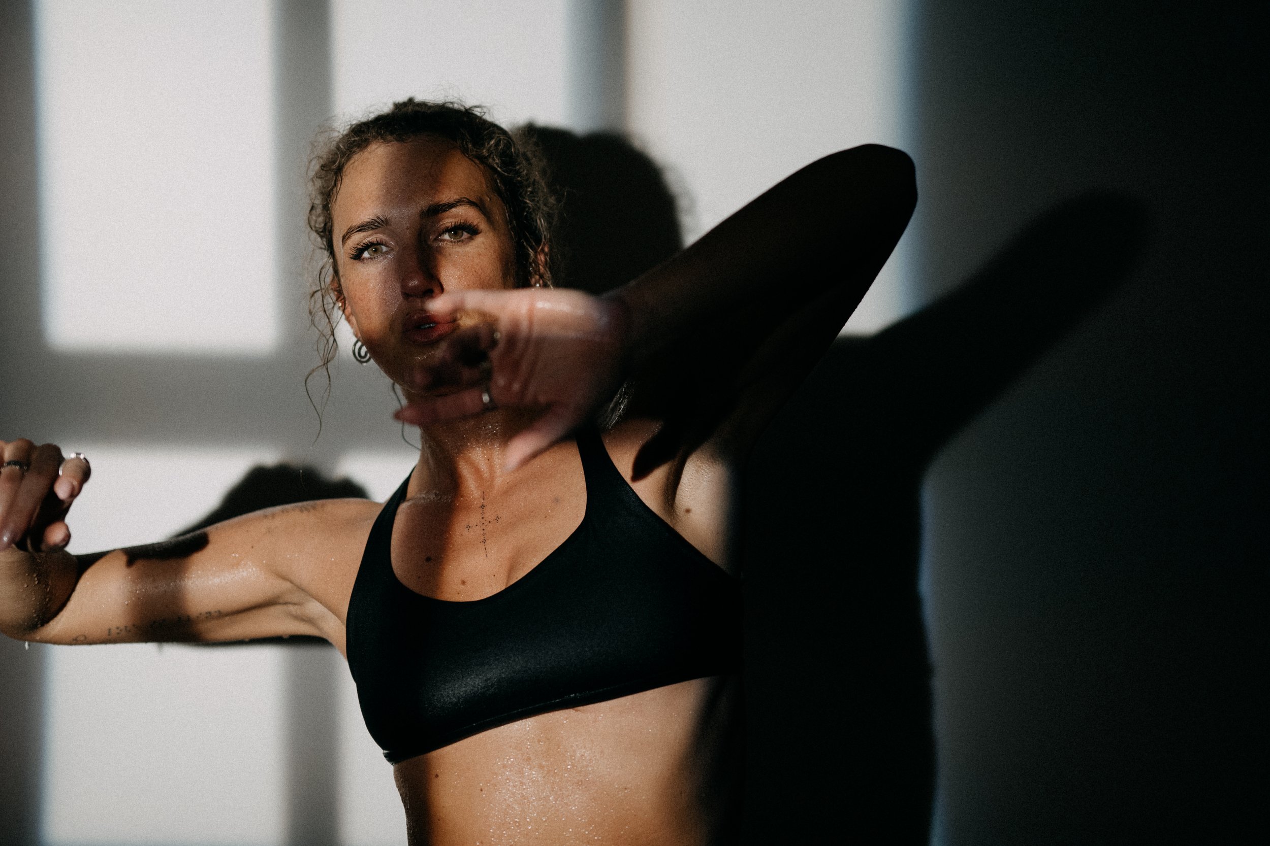 A woman in black athletic wear is striking a dynamic pose with her arm extended, with shadows and light creating a dramatic effect.