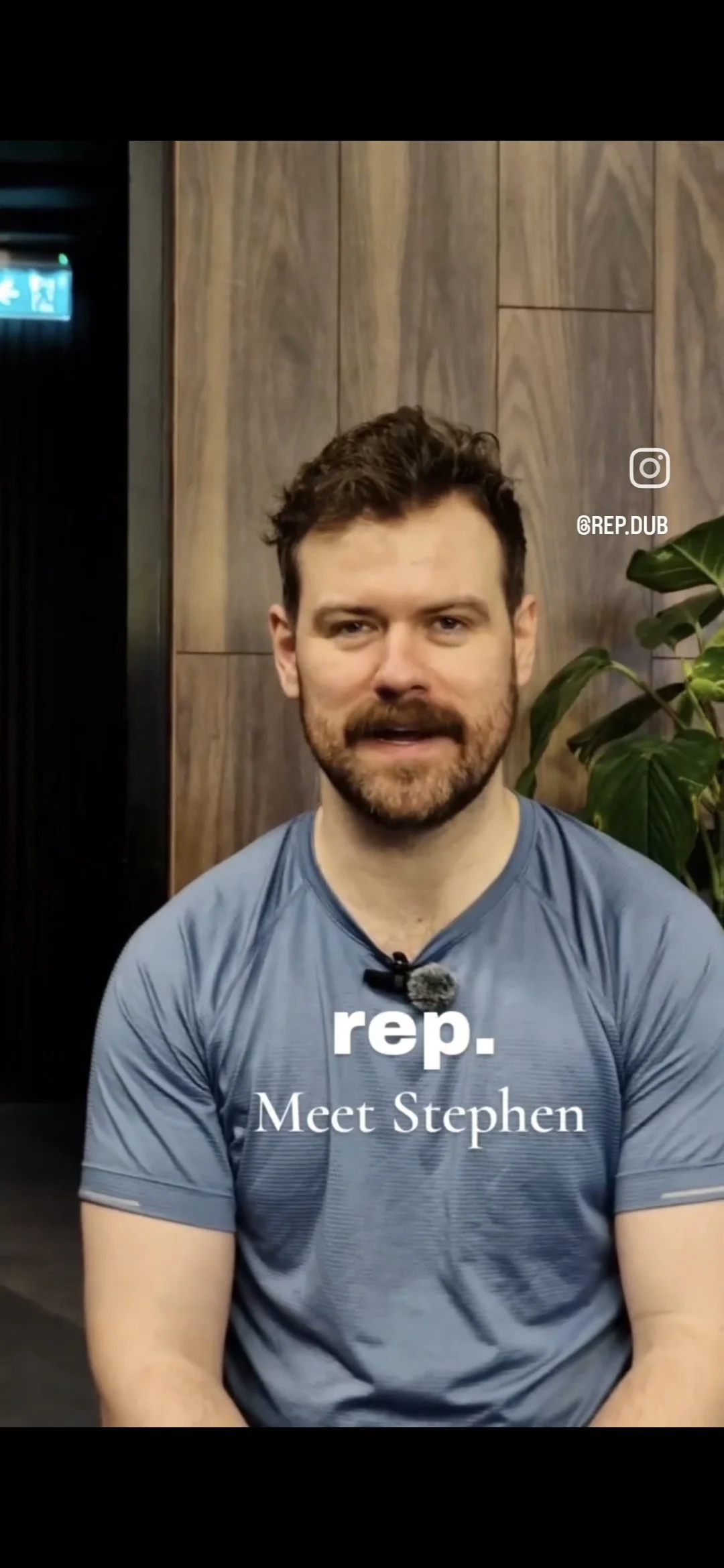 A man with dark curly hair and a beard, wearing a blue athletic shirt, sitting in front of a wooden wall with a green plant to his right. Text on the image says 'rep. Meet Stephen'.