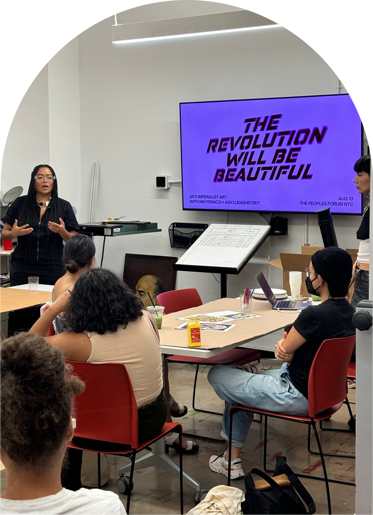 CM Fellow Niki Franco speaks in front of a sign that says "the revolution will be beautiful"