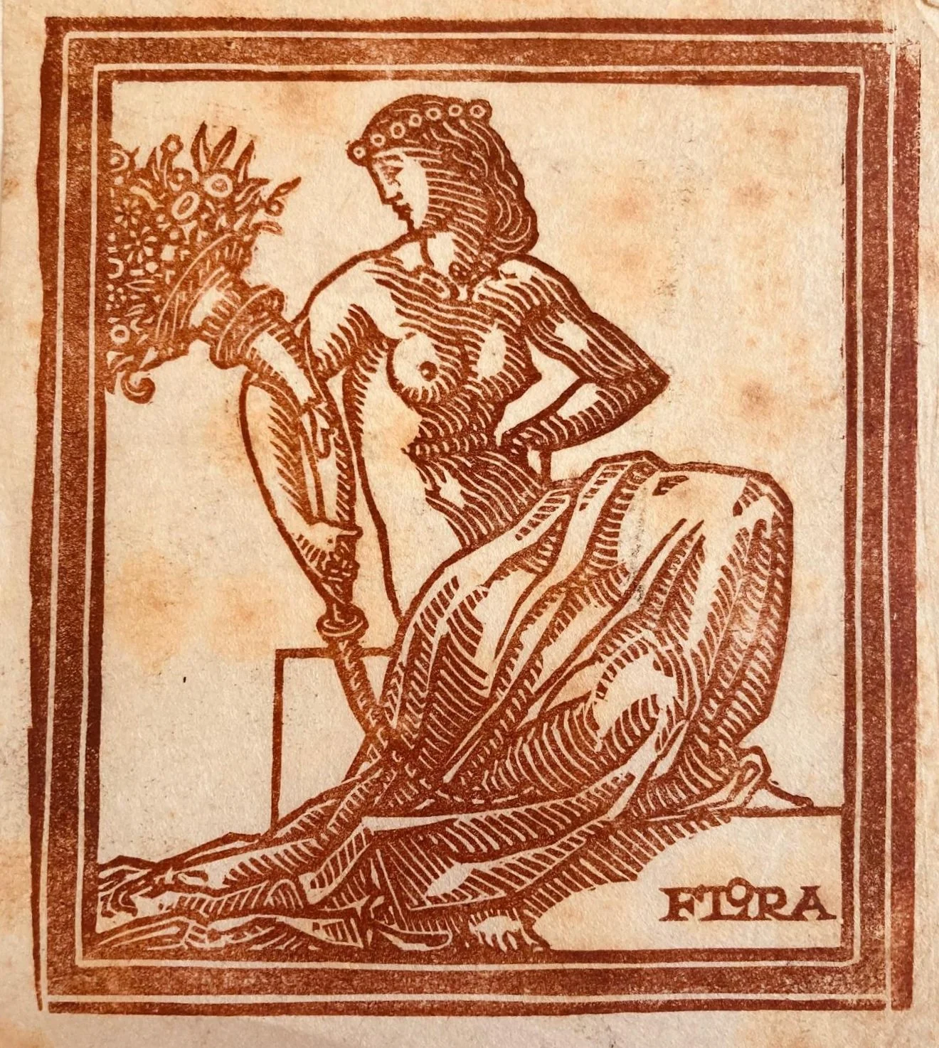 Illustrazione di una figura femminile seduta, con capelli adornati da una corona di fiori, che tiene un mazzo di fiori in una mano e l'altra mano appoggiata sui fianchi, con la scritta "FTORA" in basso a destra.