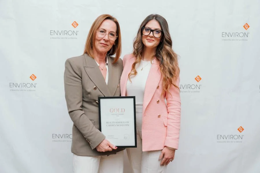 Two women posing with an award against an Environ branded backdrop.
