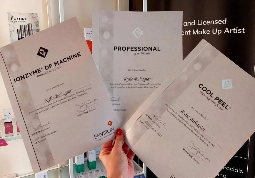 Three cosmetic training certificates held by a hand.