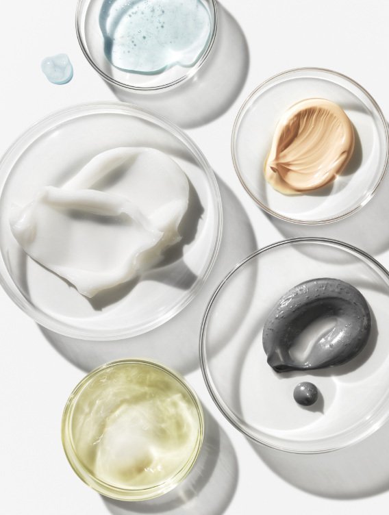 Environ skincare Malta, product textures. Assorted skincare creams and gels in glass bowls on a white surface, including white, beige, gray, clear, and light yellow substances.